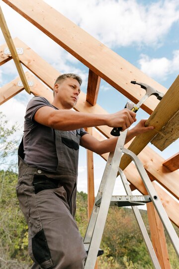 Ein Bauarbeiter steht auf einer Leiter und arbeitet an einem Holzdachgerüst.